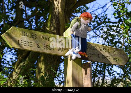 Yarnbombe Person am Fingerpfosten befestigt (öffentlicher Fernwanderweg, Ebor Way, Dales Way Link) Nahaufnahme - Menston, West Yorkshire, England Großbritannien. Stockfoto
