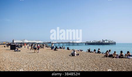 Brighton Palace Pier und Strand an einem warmen Apriltag mit Sonnensuchenden am Strand in Brighton, Sussex, Großbritannien am 27. April 2025 Stockfoto