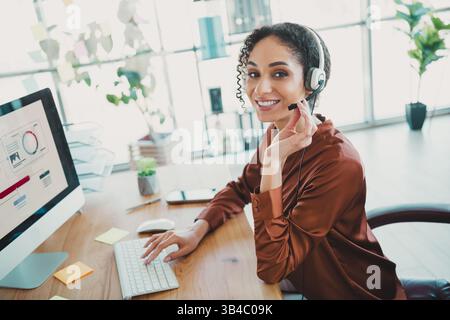 Junge professionelle Frau, die ein Headset trägt, arbeitet in Büroumgebungen, stellt Arbeitsplatztechnologie und Geschäftskommunikation vor. Stockfoto