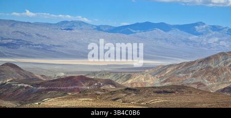 Farbenfrohe geschichtete Berge und trockene Ebenen im Death Valley, Kalifornien, mit dramatischer Geologie und Wüstenlandschaft unter klarem Himmel. Stockfoto