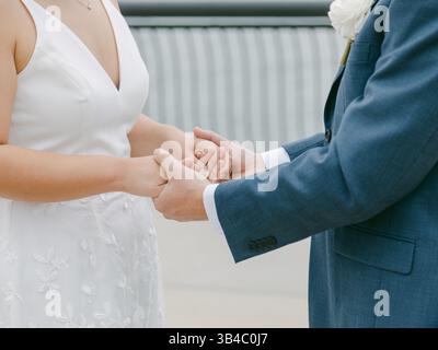 Zwei Personen teilen sich einen zärtlichen Moment, während sie in einer Hochzeitsumgebung unter klarem Himmel die Hände halten. Stockfoto