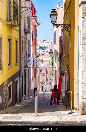 Enge kopfsteingepflasterte Straße mit traditionellen bunten Gebäuden und historischen Straßenlaternen in Lissabons Altstadt, Portugal. Stockfoto