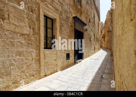 Enge, sonnendurchflutete Gasse mit Kalksteinmauern in Mdina, Malta, mit historischen Türen, Fenstern und klassischem mediterranem Charme. Stockfoto