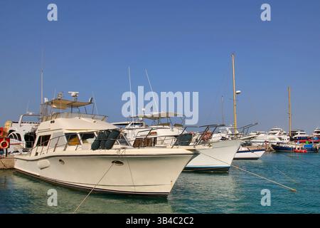 Luxusyachten im Yachthafen in Hurghada, Ägypten, mit Moscheen-Minaretten und palmengesäumter Promenade unter klarem blauen Himmel, Küstenresort-Szene am Roten Meer. Stockfoto