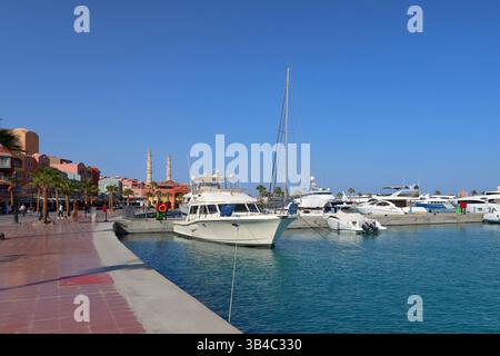 Luxusyachten im Yachthafen in Hurghada, Ägypten, mit Moscheen-Minaretten und palmengesäumter Promenade unter klarem blauen Himmel, Küstenresort-Szene am Roten Meer. Stockfoto