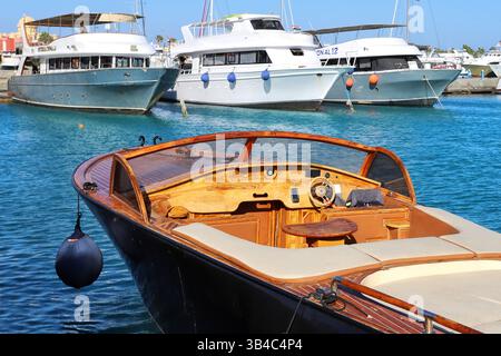 Luxusyachten im Yachthafen in Hurghada, Ägypten, mit Moscheen-Minaretten und palmengesäumter Promenade unter klarem blauen Himmel, Küstenresort-Szene am Roten Meer. Stockfoto