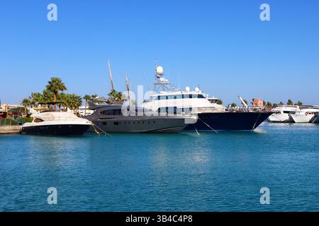 Luxusyachten im Yachthafen in Hurghada, Ägypten, mit Moscheen-Minaretten und palmengesäumter Promenade unter klarem blauen Himmel, Küstenresort-Szene am Roten Meer. Stockfoto