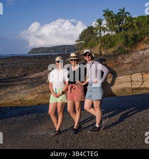 Drei Personen posieren vor einem umgestürzten Baumstamm am Strand in Panama Stockfoto