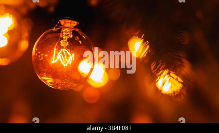 Glühlampe aus elektrischer Girlande im Retro-Stil, extreme Nahaufnahme, warmes gelbes Licht, weihnachtliche Atmosphäre Stockfoto