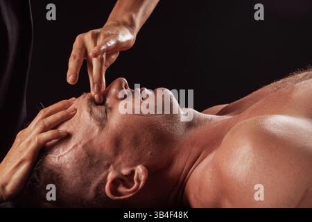 Nahaufnahme des männlichen Gesichts während der professionellen Gesichtsmassage, Therapeut unter Druck auf die Augenbrauenpartie. Stockfoto