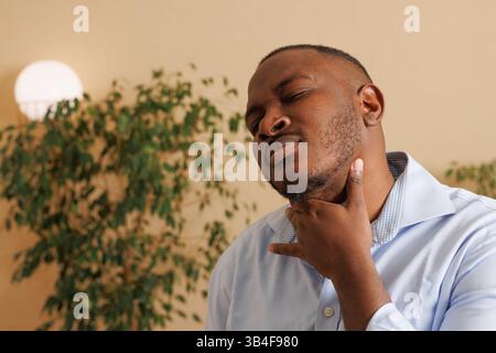 Ein Mann mit Halsschmerzen, der den Hals unangenehm hält. Konzept der Krankheit, Grippe, Erkältung, Atemwegsinfektion oder Rachenschmerzen. Inneneinrichtung, Heilung Stockfoto