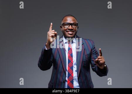 Selbstbewusster Geschäftsmann in gestreiftem Anzug und Brille, lächelt und zeigt mit beiden Händen nach oben. Konzept der Idee, des Erfolgs, der Motivation, der Führung und Stockfoto