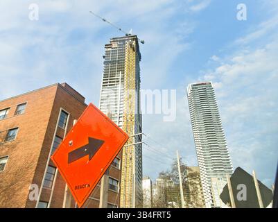 Ein beeindruckender Blick auf die Innenstadt von Toronto mit einem Wolkenkratzer im Bau, umgeben von Hochhäusern und einem orangen Richtungsschild Stockfoto