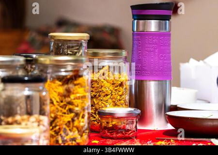 Glasgläser gefüllt mit getrockneten Kräutern und Blumen auf einem Tisch für Kräutertee, Handwerk oder natürliche Wellness-Nutzung. Stockfoto