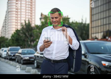 Gesichtserkennungssystem zur Identifizierung eines lächelnden Mannes mit Smartphone auf der Straße der Stadt Stockfoto