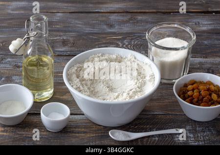 Backzutaten mit Mehl, Rosinen, Zucker, Öl, Soda, Vanillezucker und Salz auf rustikalem Holztisch, Blick von oben Stockfoto