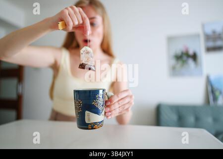 Lustiger Gesichtsausdruck einer Frau während des morgendlichen Teerituals in einem hellen, minimalistischen Raum. Stockfoto
