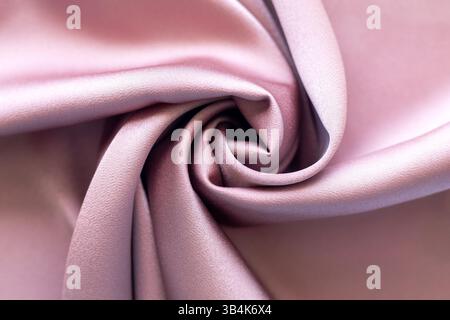 Nahaufnahme gefalteter, glänzender Stoff mit sanften Rosa-Tönen und Textur Stockfoto
