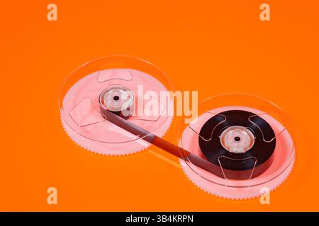 Magnetband auf Rollen einer VHS-Videokassette auf orangem Hintergrund Stockfoto