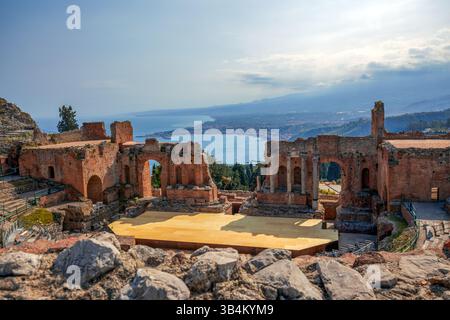 Blick auf die Säulenbühne des antiken griechischen Theaters in Taormina, Sizilien, Italien, mit atemberaubendem Blick auf das Meer und den Ätna. Stockfoto