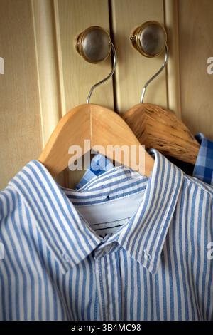 Zwei frisch gebügelte Herrenhemden auf hölzernen Kleiderbügeln, die vor den Schranktüren hängen, norfolk, england Stockfoto