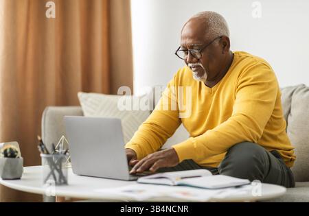Senior Black Man Eingabe Auf Laptop Online Indoor Arbeiten Stockfoto
