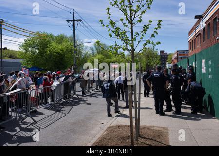 Eine Menschenmenge steht hinter Metallbarrieren, viele halten Schilder. NYPD-Offiziere stehen in Formation in der Nähe. Die Szene ist draußen, in einer Stadtstraße Stockfoto