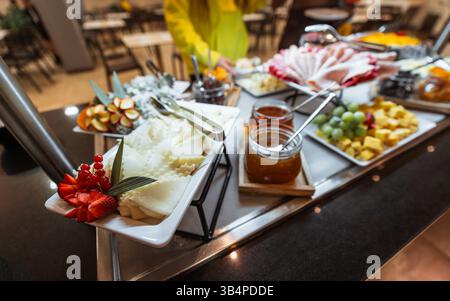 Elegantes Frühstücksbuffet mit verschiedenen Käsesorten, frischem Obst, Aufschnitt, Marmeladen in Glasgläsern und dekorativen Beilagen auf weißen Tellern Stockfoto