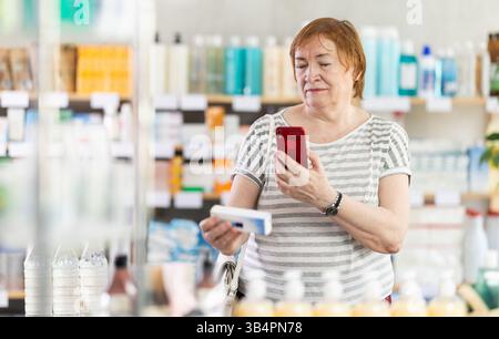 Seniorin in Apotheken scannt QR-Code auf antimykotischer Salbe Stockfoto