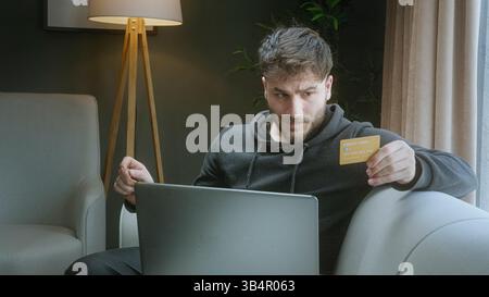 Begeisterter Mann, der den Erfolg des Online-Kaufs feiert, während er eine Kreditkarte hält und zu Hause ein Notebook verwendet Stockfoto