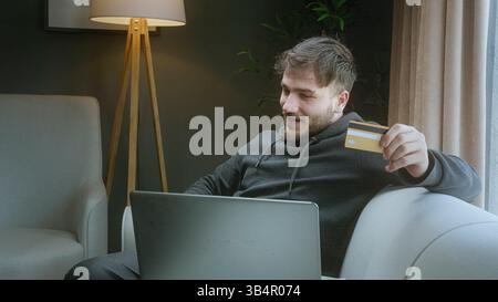 Mann feiert den Erfolg des Online-Kaufs, während er eine Kreditkarte hält und zu Hause ein Notebook verwendet Stockfoto