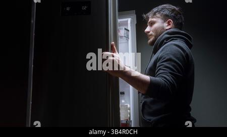 Mann sucht nach Essen im Kühlschrank und findet nicht, was er nachts will Stockfoto