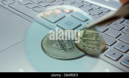 Nahaufnahme physischer Bitcoins unter Vergrößerungsglas auf Laptop-Tastatur, die die digitale Währungsanalyse darstellt Stockfoto