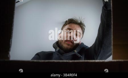 Junger Mann, der Umzugskartons zu Hause packt, POV aus dem Inneren der Box Stockfoto