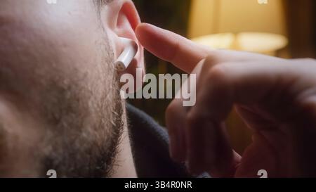 Nahaufnahme eines Mannes, der kabellose Ohrstöpsel aufsetzt, um Musik zu hören oder einen Anruf in Innenräumen zu tätigen Stockfoto