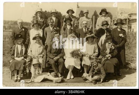Originales Vintage-Foto aus den 1920er Jahren Porträt der Arbeiterhochzeit im Freien in einem Garten, Flapper-Ära, attraktives verheiratetes Paar, Paare - schöne Braut, Bräute mit langem Schleier und Kopfschmuck, weißes Brautkleid, neben dem Bräutigam sitzend. Die Ehrenmädchen sitzen neben der Braut und dem Bräutigam. Hübscher Blumenstrauß, Blumensträuße. Die Hochzeitsgäste tragen modische Cloche-Hüte. Mann und Frau aus den 1920er Jahren. Ehemänner und Ehefrauen des Fotografen S. S. Harrison, 21 Tontine St. Folkestone, Kent, Großbritannien. Um 1925 Stockfoto
