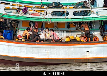 Rayong, Thailand, 26. Oktober 2024: Eine Gruppe von Arbeitern auf einem Fischerboot essen zu Mittag, während eine andere steht und arbeitet. Stockfoto