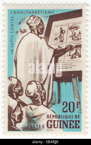 GUINEA - 19. September 1962: 20-Franken-blaue und dunkelbraune Briefmarke mit der Darstellung der Erwachsenenklasse in der Schule. Kampagne gegen Analphabetentum. Alphabetisierung im weitesten Sinne beschreibt „besondere Arten des Denkens und des Schreibens“ mit dem Ziel, Gedanken oder Ideen in schriftlicher Form in einem bestimmten Verwendungskontext zu verstehen oder auszudrücken. Mit anderen Worten, Menschen in literarischen Gesellschaften haben eine Reihe von Praktiken, um Schreiben zu produzieren und zu konsumieren, und sie haben auch Überzeugungen über diese Praktiken Stockfoto