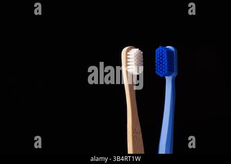 Zwei Zahnbürsten, eine aus Bambus und die andere aus blauem Kunststoff, auf schwarzem Hintergrund. Umweltprobleme. Stockfoto