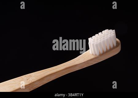 Bambus-Holzzahnbürste mit weißen Borsten auf schwarzem Hintergrund. Umweltprobleme. Minimalismus. Stockfoto
