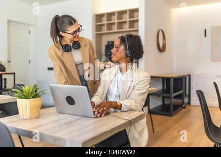 Zwei weibliche Kollegen arbeiten an einem Projekt zusammen und demonstrieren Teamarbeit und Unterstützung in einem modernen Arbeitsbereich Stockfoto