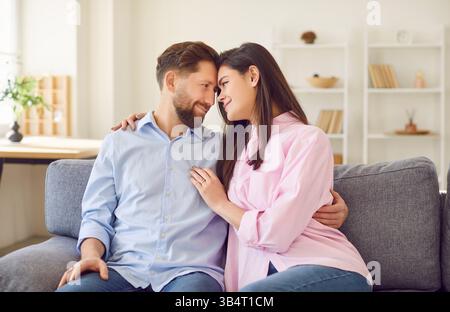 Junge glückliche verheiratete Paare sitzen auf dem Sofa im Wohnzimmer zu Hause und lächeln. Stockfoto