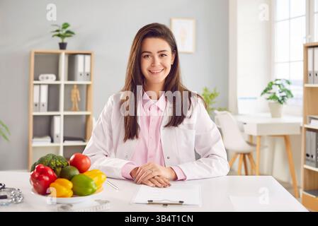 Porträt einer fröhlichen jungen freundlichen Ärztin-Ernährungsberaterin, die am Arbeitsplatz im Büro sitzt. Stockfoto