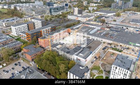 Blick aus der Vogelperspektive auf ein modernes Stadtgebiet mit Wohn- und Geschäftsgebäuden, umgeben von Grün und Parkplätzen. Die Architektur ist zeitgenössisch Stockfoto