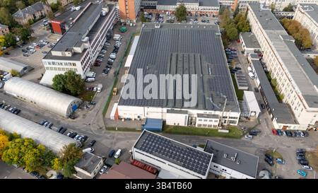 Luftaufnahme eines Industriekomplexes mit Solarpaneelen auf Dächern, umgeben von Straßen und geparkten Autos. Stockfoto