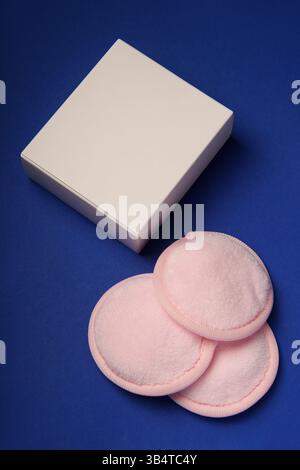 Weiße Box und drei wiederverwendbare pinkfarbene Schminkpads aus Baumwolle auf blauem Hintergrund. Der Begriff der Ökologie und des bewussten Konsums. Wiederverwendbare Festplatten. Stockfoto