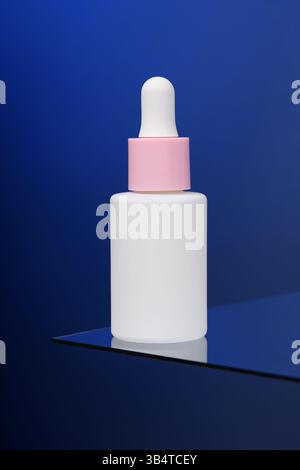 Auf dem blauen Hintergrund steht eine Flasche Serum auf Glas. Vertikales Werbefoto von Kosmetika. Modell. Vorlage. Stockfoto