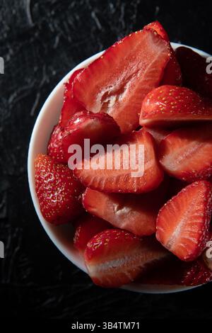 Rote reife Erdbeeren in einer Untertasse auf schwarzem Hintergrund in Nahaufnahme. Stockfoto