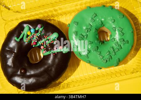 Zwei Donuts Schokolade und Grün auf gelbem Hintergrund in einer Box Nahaufnahme. Horizontales Studio-Foto. Stockfoto