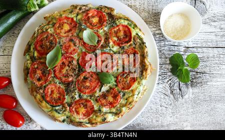 Hausgemachte, im Ofen gebackene Frittata mit Gemüse wie Zucchini, Tomaten, Eiern und Basilikum. Gesunde Ernährung. Sommeressen. Direkt darüber. Stockfoto